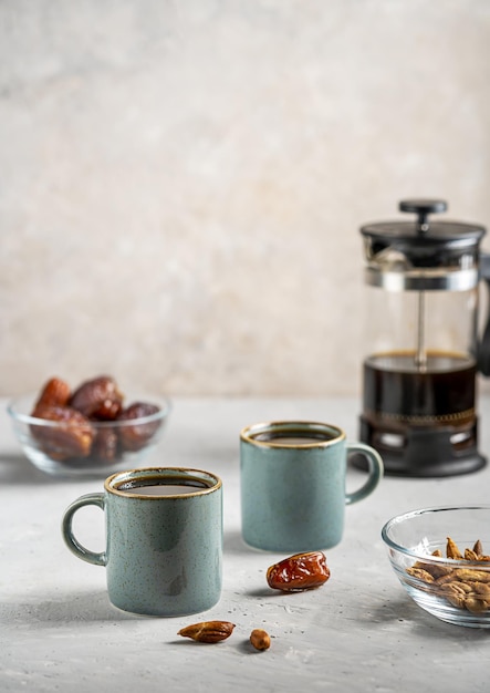 Café de semilla de dátil saludable en dos tazas de café con dátiles, frutas y semillas sobre fondo gris