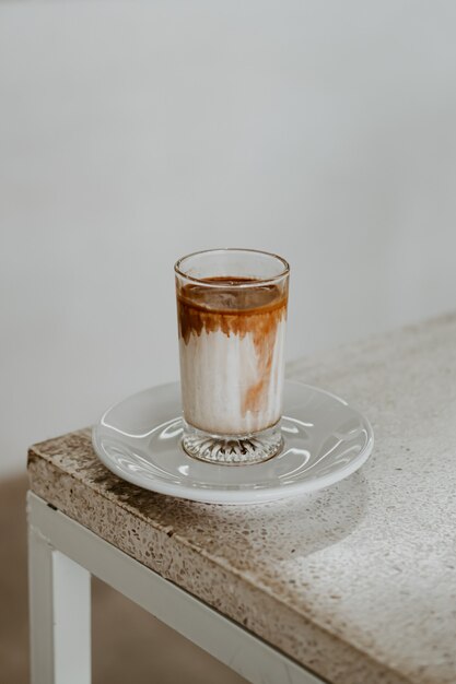 Café sucio en un vaso colocado sobre una mesa blanca con luz solar por la mañana.