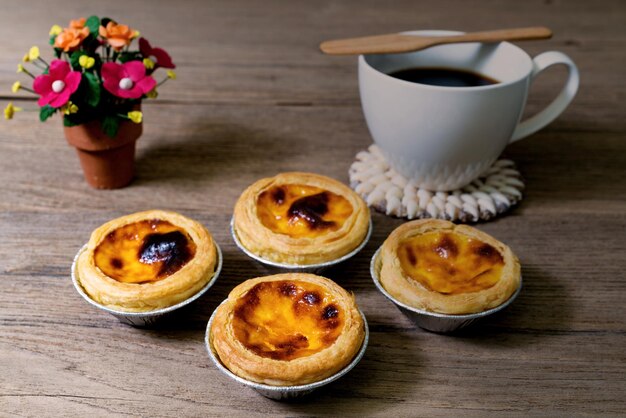 café con tarta de huevo en una taza de papel de aluminio en una mesa de madera