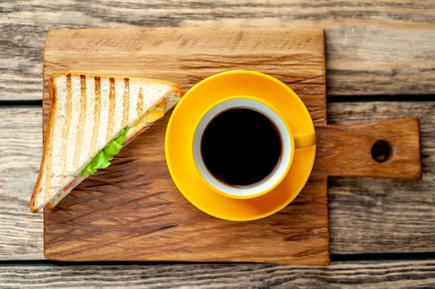 café en una taza amarilla y sandwich en una tabla para cortar