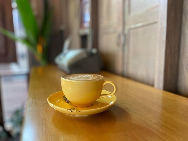 Café en una taza amarilla sobre una mesa de madera en un café con fondo decorativo