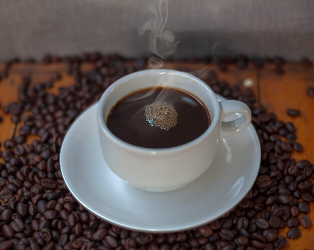 Café en una taza blanca y granos de café en una mesa de madera