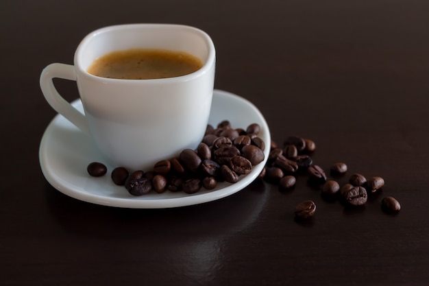 Foto café en una taza blanca y granos de café sobre la mesa