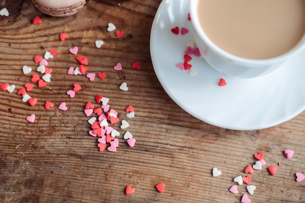 Café en una taza blanca sobre un fondo de madera salpicado de corazones