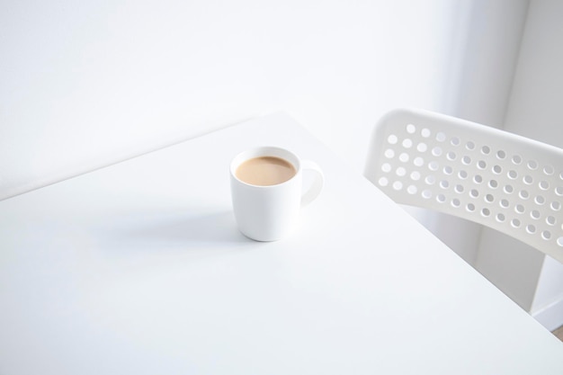Café en una taza blanca sobre una mesa blanca bajo luz natural
