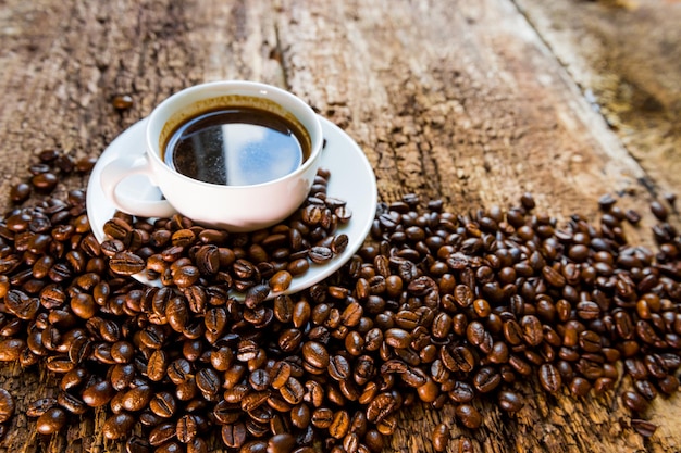 Café Una taza de café caliente y granos de café tostados en una mesa de madera Fondo oscuro