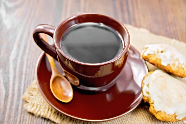 Café en taza marrón con galletas de calabaza en una servilleta de un saqueo sobre un fondo de tablones de madera oscura.