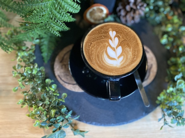 Café en taza negra en la mesa de madera en café con planta.