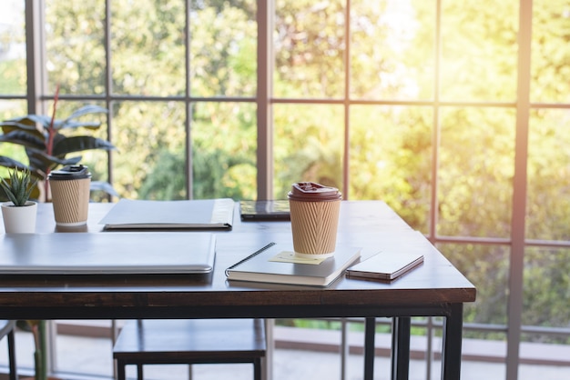 Café en taza de papel, portátil y portátil en la mesa de madera en la oficina