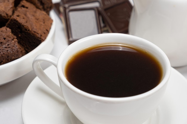 Café en una taza de pastel de chocolate y trozos de chocolate sobre un fondo blanco