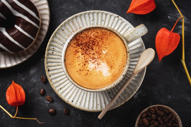 Café en una taza con una rosquilla, granos de café y flores de Physalis