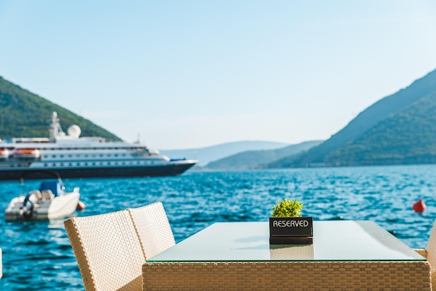 Café-Tisch am Strand mit schöner Aussicht auf das Meer und die Berge reservierte Platte darauf Kreuzfahrtschiff im Hintergrund