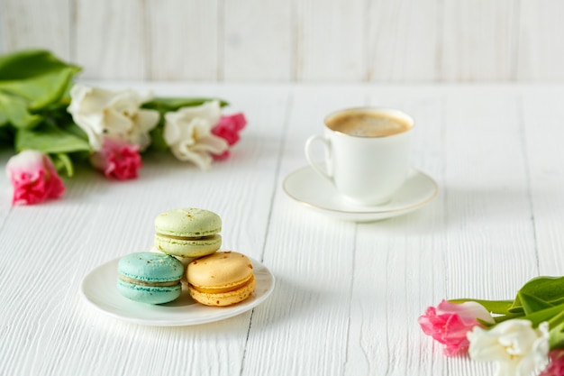 Café, tulipanes rosados y blancos y macarons en la mesa de madera blanca. Desayuno. Descanso.