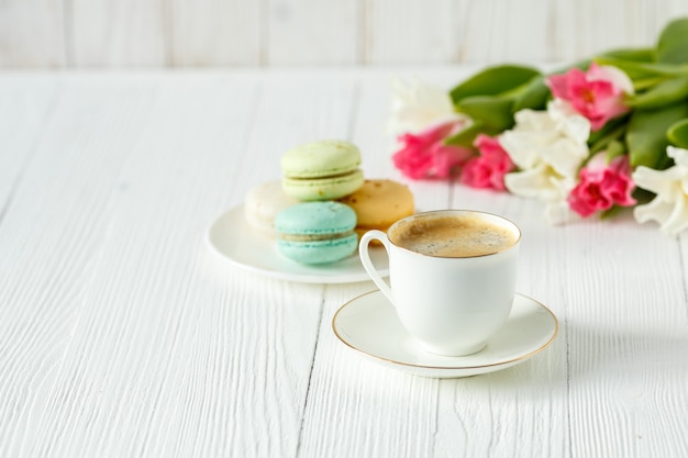 Café, tulipanes rosados y blancos y macarons en la mesa de madera blanca. Desayuno. Descanso.