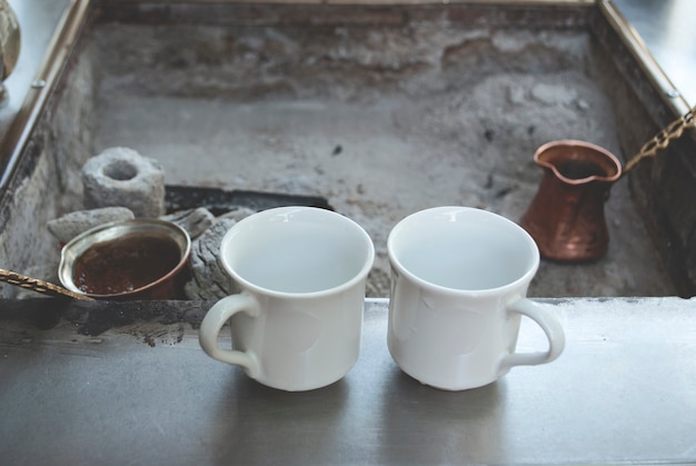 Café turco al carbón. El café se prepara sobre brasas en un cezve de café turco. Dos tazas se colocan en la superficie cerca de las brasas.