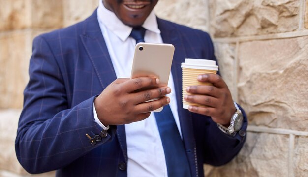 Café de viaje y manos de hombre de negocios con teléfono en viaje a pie para correo electrónico de redes sociales o comercio electrónico Tecnología Internet y hombre negro corporativo en descanso al aire libre con conexión móvil 5g