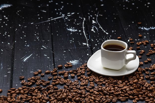 El café se vierte en una taza sobre una mesa de madera negra con granos de café.