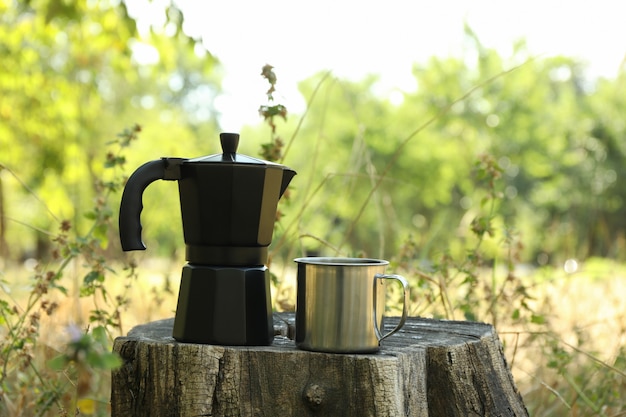 Cafeteira e copo de metal no toco ao ar livre