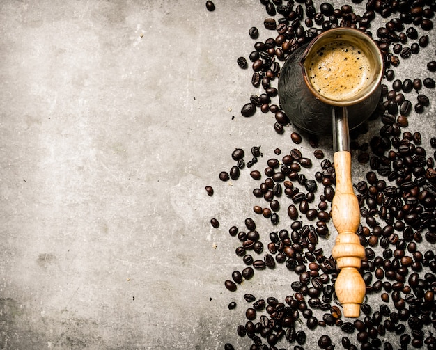 Cafetera y café tostado alrededor. Sobre un fondo de piedra.