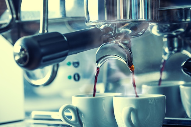Foto cafetera de cromo que prepara un delicioso café en dos tazas blancas. sale vapor de las tazas.