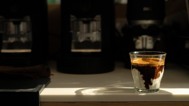 Una cafetera está en un mostrador con un vaso de café.