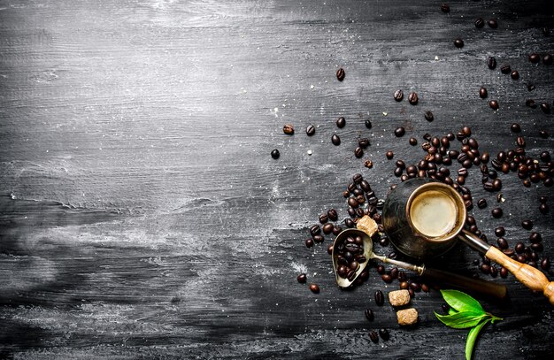 Cafetera con granos de café, azúcar de caña y hojas frescas. En una pizarra negra.