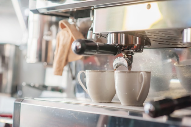 Cafetera haciendo y vertiendo en taza blanca.