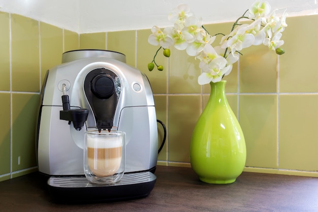 Cafetera con un latte macchiato en una acogedora casa decorativa con paredes verdes y flores. café casero