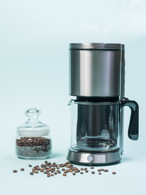 Cafetera y tarro de cristal con granos de café sobre un fondo azul. El concepto de un desayuno clásico.