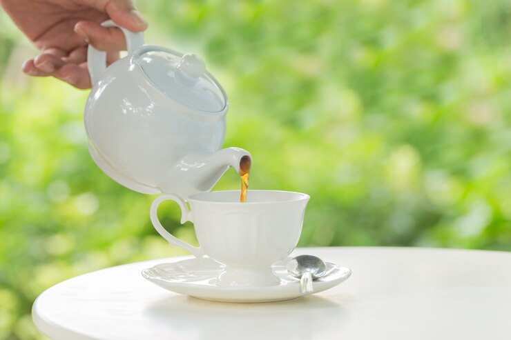 Cafetera verter café caliente en una taza durante el desayuno en la luz del sol de la mañana