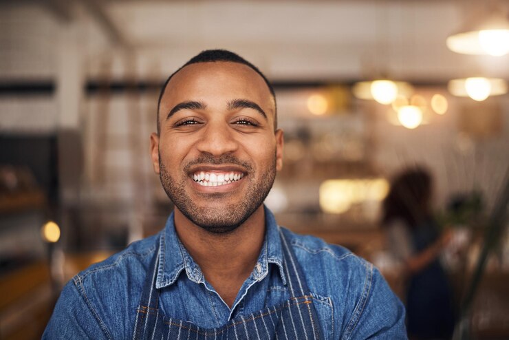 Foto cafeteria garçom feliz e retrato de homem negro no restaurante para serviço trabalhando e sorria no café inicialização de bistrô de pequeno empresário e rosto de garçom no refeitório pronto para servir