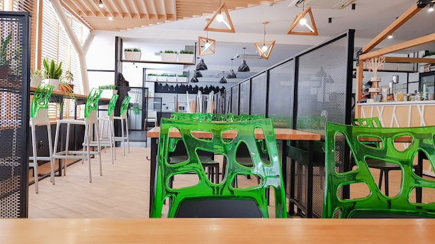 Cafeteria, kein Esszimmer mit Holztischen und grünen Stühlen. Interieur mit Holz- und Metallelementen. Moderne Essbereiche mit Fensterbeleuchtung. Ukraine, Kiew - 19. Februar 2021.