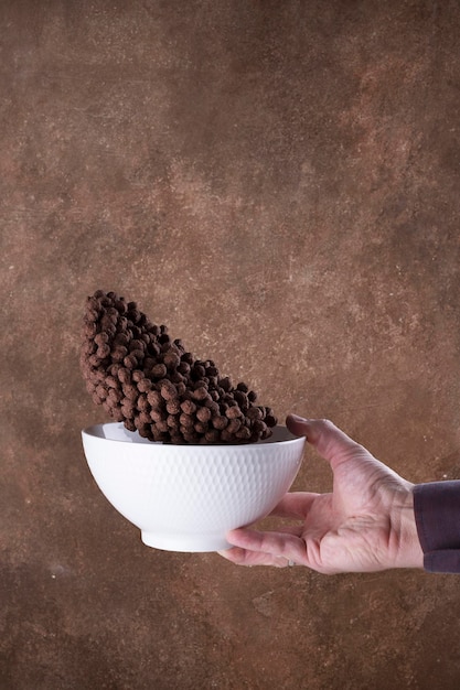 Caída de bolas de chocolate en un recipiente blanco sobre fondo marrón. levitación.