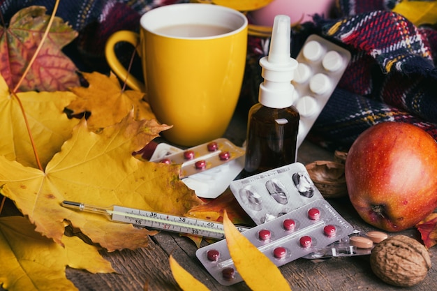 Caída y cuidado de la salud. Taza de té, pastillas y termómetro sobre un fondo de madera