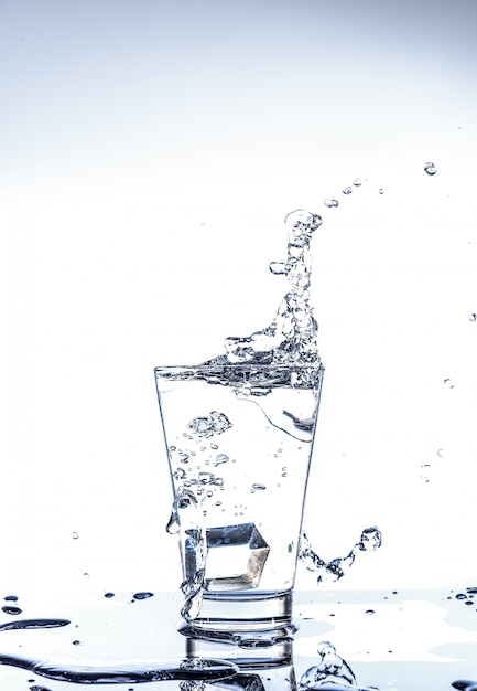 Caída de hielo y salpicaduras de agua en el vaso con reflejo en la mesa del espejo