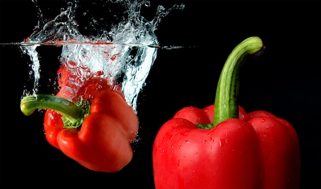 Caída de pimiento y salpicaduras de agua con fondo negro.