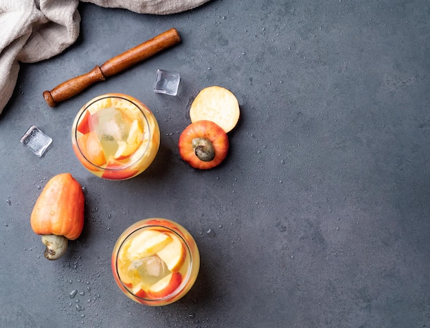 Caipirinha de caju brasileira em copos com gelo e fatias de frutas sobre fundo de pedra com espaço de cópia