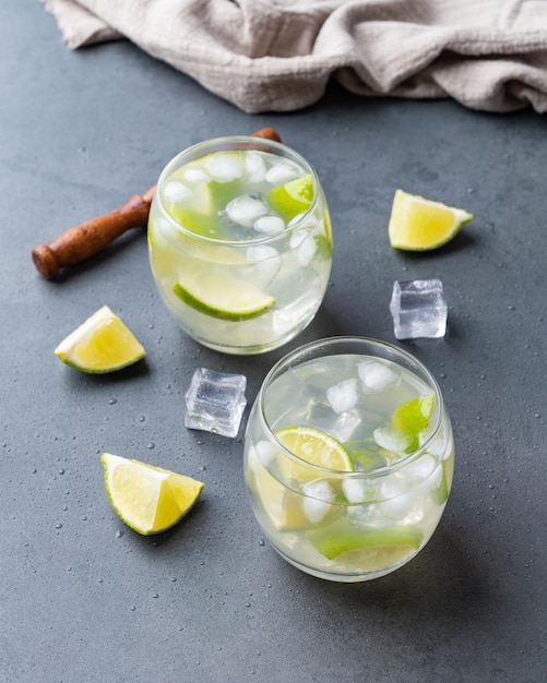 Caipirinha de limão brasileiro em copos com gelo e fatias de frutas sobre fundo de pedra