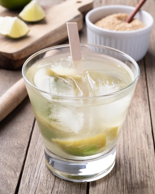 Caipirinha de limão brasileiro em um copo com gelo e frutas sobre a mesa de madeira