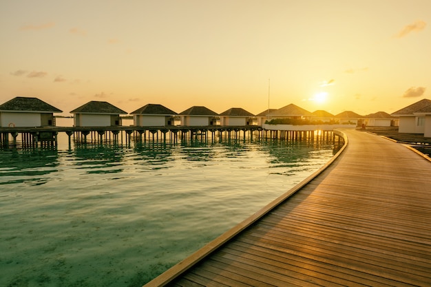 Cais de madeira e linha de moradias tropicais na hora do nascer do sol, Maldivas