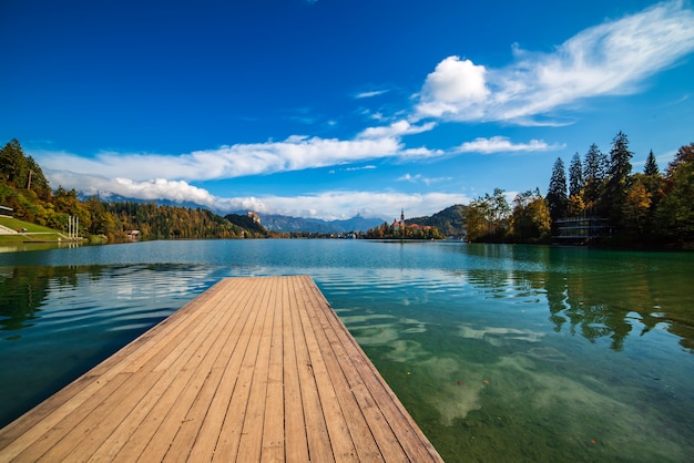 Foto cais de madeira lago bled, eslovênia, com céu azul e nuvens no outono