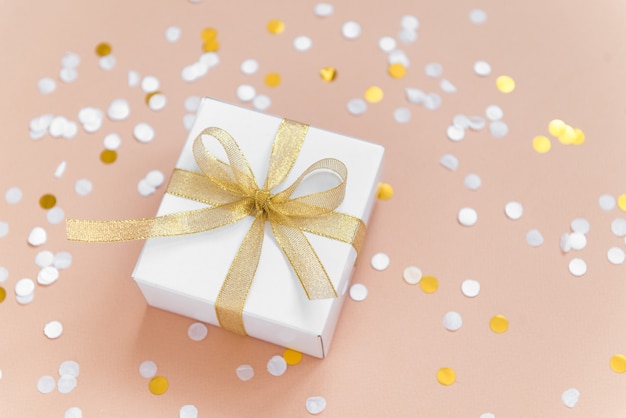 caixa branca com fita para presente de Natal com confete plano deitado sobre fundo bege