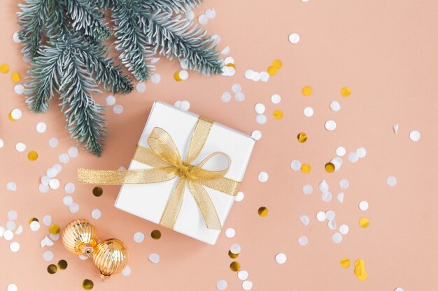 caixa branca para presente de Natal em fundo bege com bolas de confete douradas e pinheiros