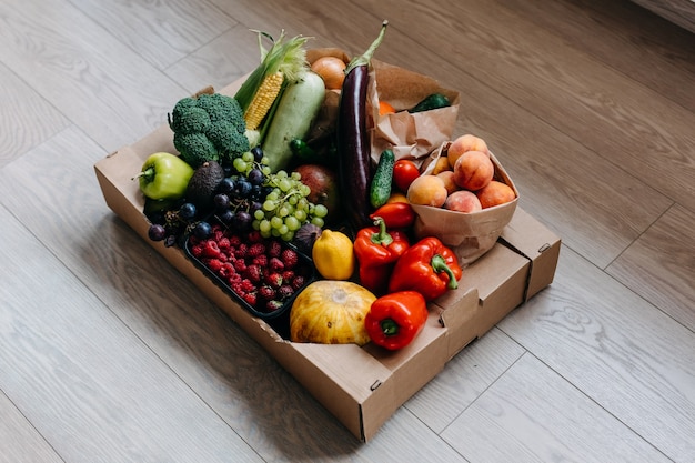 Caixa cheia de vários vegetais orgânicos, frutas e bagas no chão conceito de entrega de comida