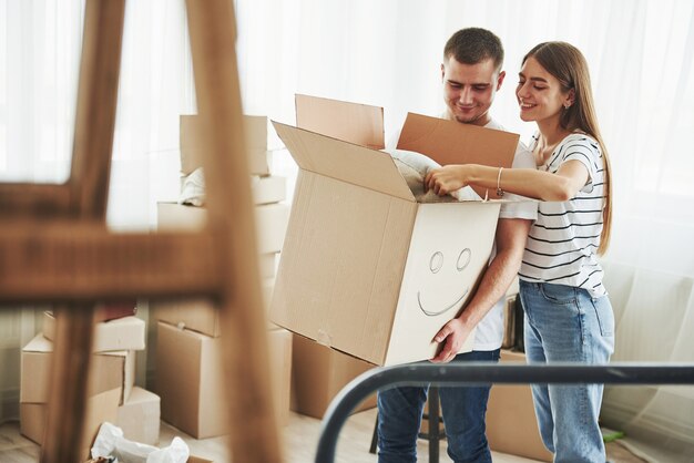 Caixa com um sorriso pintado. casal jovem alegre em seu novo apartamento. concepção de movimento.