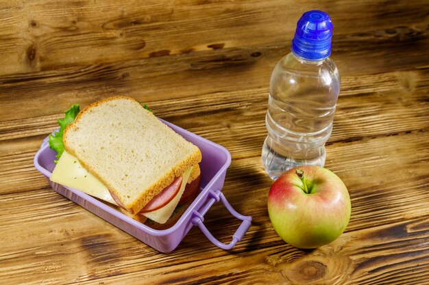 Foto caixa de almoço com sanduíches garrafa de água e maçã em uma mesa de madeira