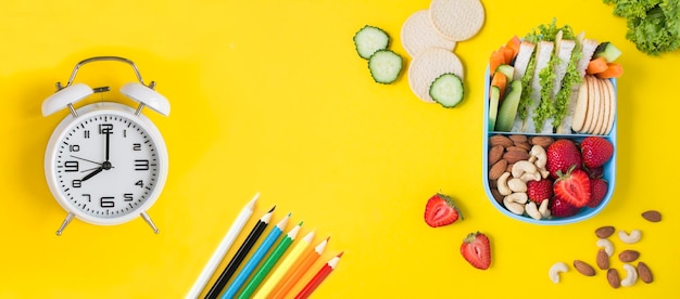 Foto caixa de almoço da escola despertador branco e lápis de cor no fundo amarelo vista superior espaço de cópia