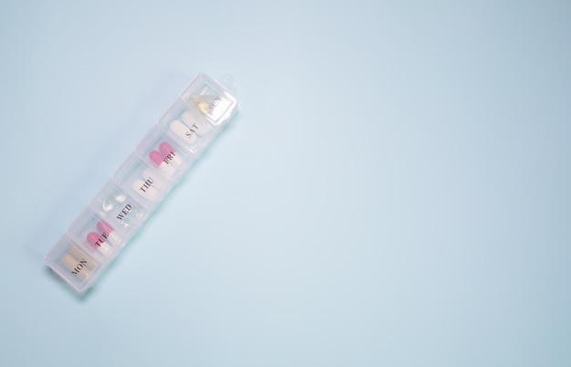Caixa de comprimidos diária com comprimidos médicos isolados em fundo azul com espaço de cópia para o seu texto.