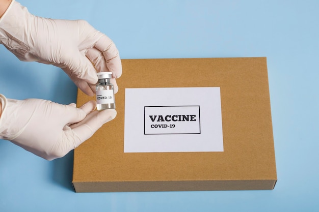 Caixa de conceito médico com vacina de coronavírus. A mão de um médico em uma luva branca segura um frasco da vacina ou remédio covid 19 sobre um fundo azul.