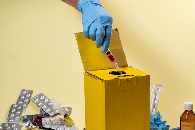 Caixa de descarte amarela para produtos contaminados ou infecciosos em um hospital ou em casa. Mão colocando uma seringa